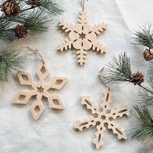 May include: Three wooden snowflake ornaments with intricate cutouts. The snowflakes are a light brown color and have a rustic, handmade look.