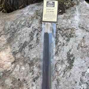 May include: A package of incense sticks, "Spirit of the Wind," with a label featuring a mountain scene. The incense is dark in color and is packaged in a clear plastic sleeve. The background is a gray rock surface.