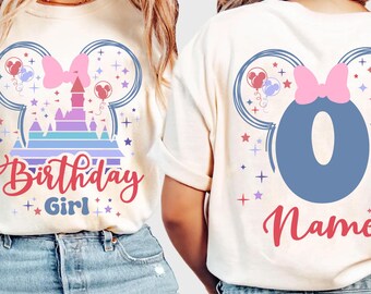 May include: Ivory-colored t-shirts with a colorful graphic design. The front features a castle, bow, and the words "Birthday Girl." The back displays a large number "0" and the word "Name." The design includes Mickey Mouse ears and balloons.