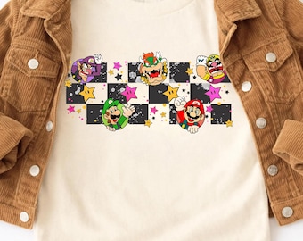 May include: Cream-colored t-shirt featuring a colorful graphic of various Mario characters, including Mario, Luigi, and Bowser, set against a black and white checkered pattern with stars. The shirt is paired with a brown corduroy jacket.