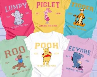May include: A collection of colorful t-shirts featuring characters from Winnie the Pooh. Each shirt displays a character's name, such as "Lumpy," "Piglet," and "Tigger," along with the year "1926" and the phrase "Winnie the Pooh."