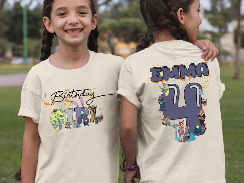 K&ouml;nnte beinhalten: Hellbeige T-Shirt mit der Aufschrift "Birthday Girl" und einer Cartoon-Grafik auf der Vorderseite. Auf der R&uuml;ckseite des Shirts stehen der Name "EMMA" und die Zahl "4" mit Cartoon-Figuren. Das Shirt ist f&uuml;r einen Geburtstag.