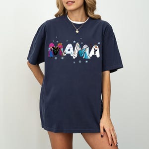 May include: Navy blue t-shirt with the word "MAMA" in a whimsical font, each letter featuring characters from a popular animated film. The design includes snowflakes, creating a playful and thematic look.