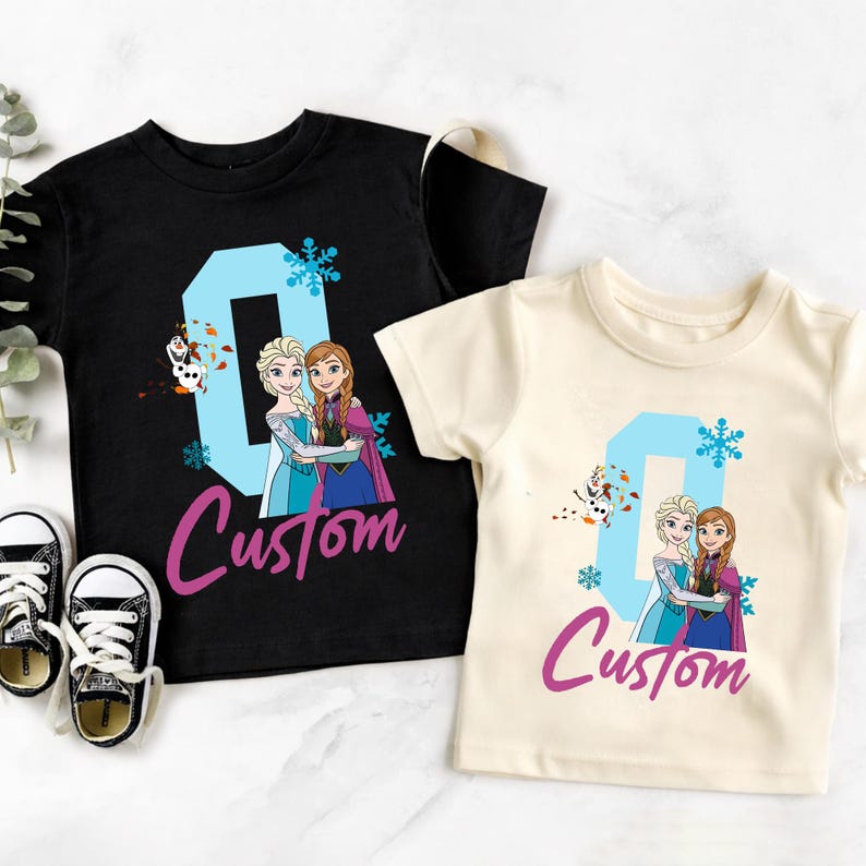 May include: Two short-sleeved t-shirts, one black and one cream, featuring a graphic of two cartoon princesses and the number "0" in light blue. The word "Custom" is written in a cursive font.
