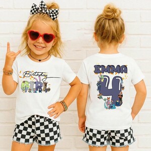 K&ouml;nnte beinhalten: Zwei wei&szlig;e T-Shirts mit Geburtstagsthema. Auf einem Shirt steht "Birthday Girl" mit bunten Cartoon-Figuren. Das andere Shirt hat den Namen "Emma" und die Zahl "4" mit Cartoon-Figuren. Das M&auml;dchen tr&auml;gt karierte Shorts und eine Sonnenbrille.