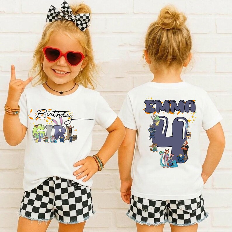 K&ouml;nnte beinhalten: Zwei wei&szlig;e T-Shirts mit Geburtstagsthema. Auf einem Shirt steht "Birthday Girl" mit bunten Cartoon-Figuren. Das andere Shirt hat den Namen "Emma" und die Zahl "4" mit Cartoon-Figuren. Das M&auml;dchen tr&auml;gt karierte Shorts und eine Sonnenbrille.