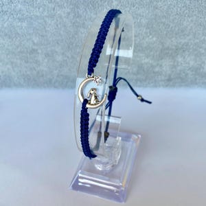 K&ouml;nnte beinhalten: Ein marineblaues Freundschaftsarmband mit einem silbernen Anh&auml;nger in Form einer Mondsichel mit einem Stern und einem darauf sitzenden Hasen.