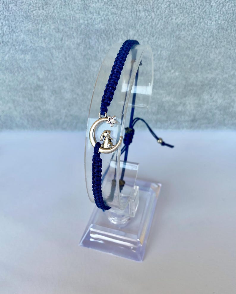 K&ouml;nnte beinhalten: Ein marineblaues Freundschaftsarmband mit einem silbernen Anh&auml;nger in Form einer Mondsichel mit einem Stern und einem darauf sitzenden Hasen.