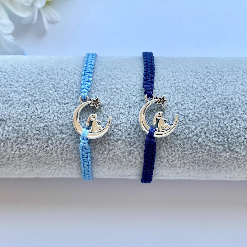 K&ouml;nnte beinhalten: Zwei Freundschaftsarmb&auml;nder mit einem silbernen Anh&auml;nger eines Kaninchens, das auf einem Halbmond sitzt. Ein Armband ist hellblau und das andere dunkelblau.
