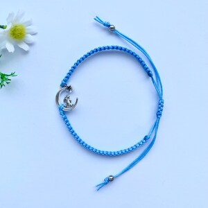K&ouml;nnte beinhalten: Ein hellblaues geflochtenes Armband mit einem silbernen Anh&auml;nger eines Kaninchens, das auf einem Halbmond sitzt.