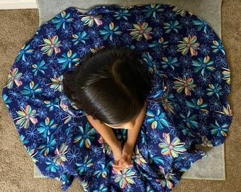 May include: A full-skirted dress in a deep navy blue fabric featuring a repeating pattern of stylized flowers in shades of bright turquoise, yellow, orange, and white. The garment displays a wide, flared silhouette with a dense floral print.