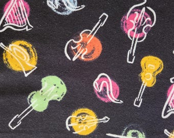 May include: Black fabric with a repeating pattern of musical instruments. The design includes white outlines of guitars, harps, and other stringed instruments, with colorful, textured backgrounds in yellow, orange, pink, and green.