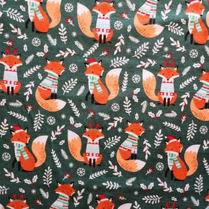 May include: A repeating pattern of cartoon foxes in festive attire, including sweaters, scarves, and Santa hats, set against a dark green background with white foliage and snowflakes. The foxes are orange and white.