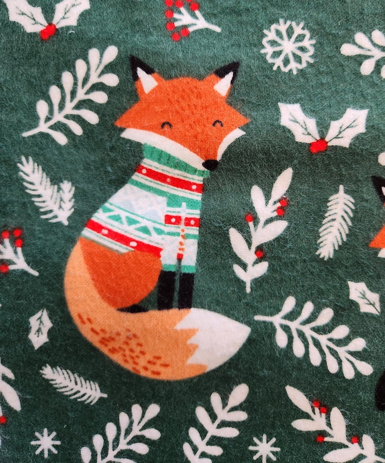 May include: A festive green fabric featuring a cartoon fox wearing a sweater with red, white, and green patterns. The design includes white snowflakes, holly, and sprigs, creating a holiday theme.