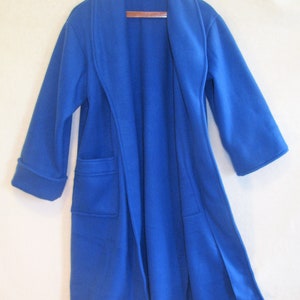 May include: A royal blue robe with a shawl collar and two front pockets hangs on a wooden hanger. The robe has long sleeves with folded cuffs and a knee-length hem. The open front design is visible.