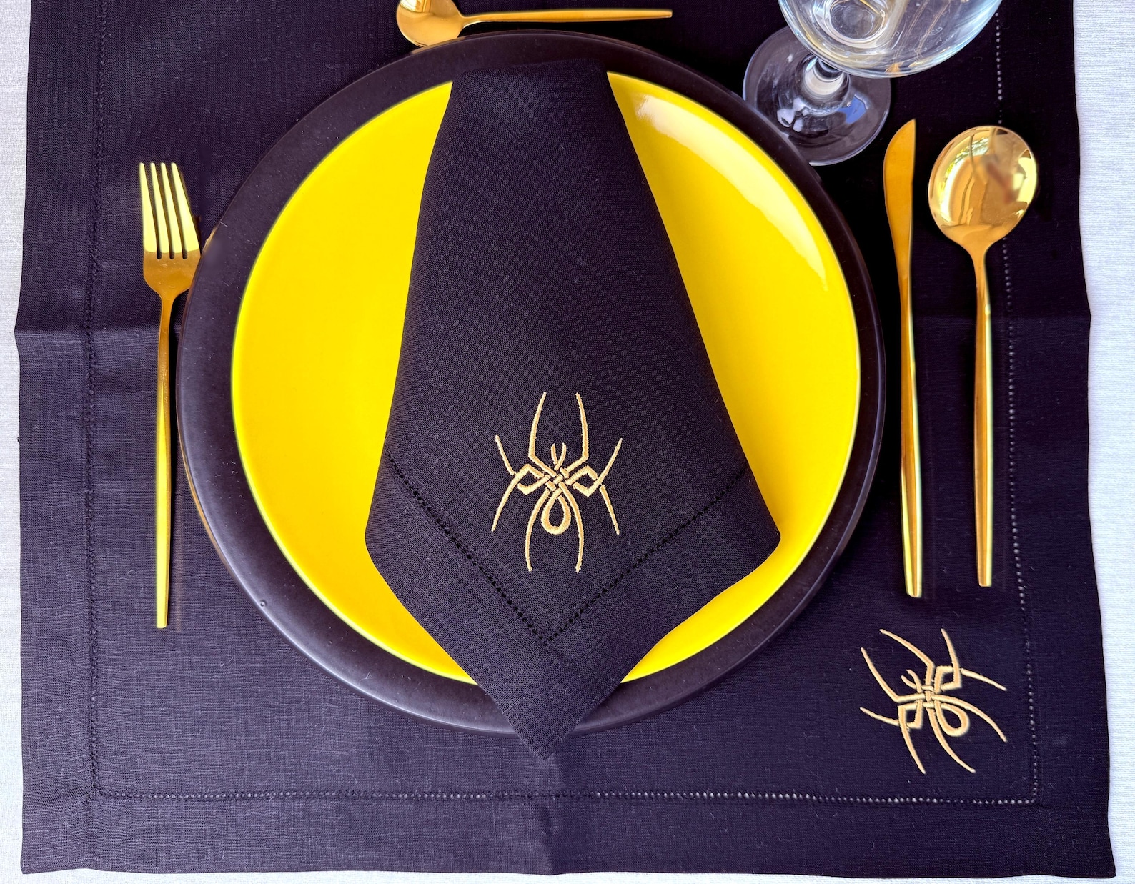 A Gold Spider on a Dark Fold Black embroidered spider napkin folded on a bright yellow plate.