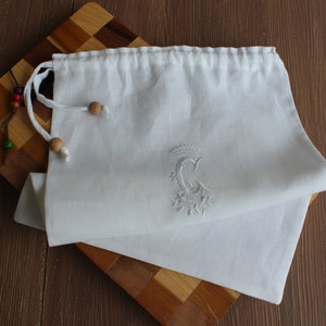 May include: White linen drawstring bag with a white embroidered letter C and a crown above it.