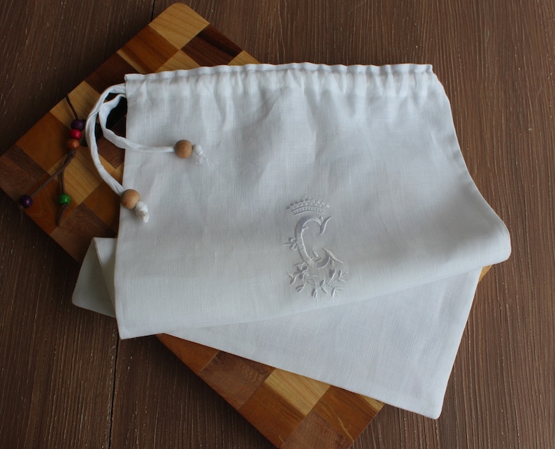 May include: White linen drawstring bag with a white embroidered letter C and a crown above it.
