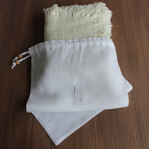 May include: White linen drawstring bag with a white embroidered letter "C" with a crown and floral design.