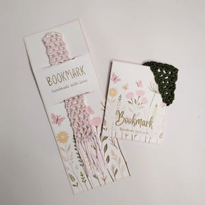 May include: A light pink crocheted bookmark with a tassel on a floral card labeled BOOKMARK handmade with love, and a dark green triangular crocheted corner bookmark on a floral card labeled Bookmark handmade with love.