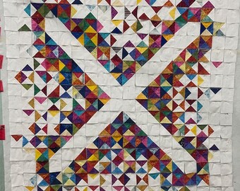 May include: A quilt with a white background and a pattern of colorful triangles arranged in a geometric design. The triangles are in various shades of red, blue, green, yellow, and purple.