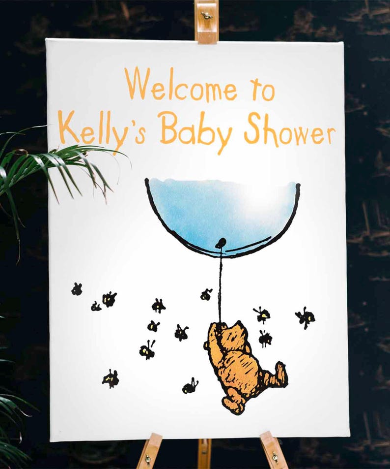 Puede incluir: Un cartel blanco con el texto "Welcome to Kelly's Baby Shower" en letras naranjas. Una ilustraci&oacute;n de dibujos animados de Winnie the Pooh sujetando un globo azul con abejas volando a su alrededor.