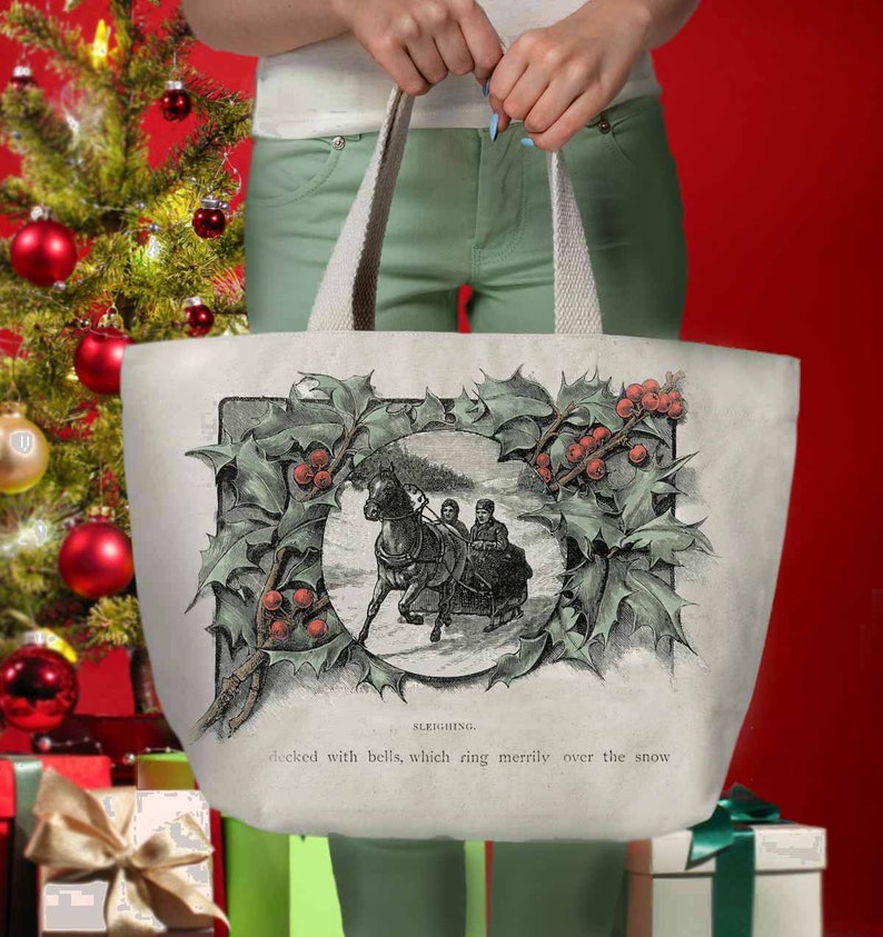 May include: A white canvas tote bag with a vintage illustration of a horse-drawn sleigh surrounded by a holly wreath. The text "SLEIGHING. decked with bells, which ring merrily over the snow" is printed below the image.
