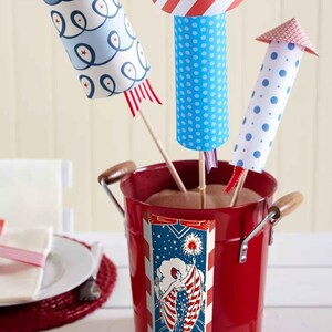 Peut inclure: Trois d&eacute;corations de p&eacute;tards en papier dans un seau en m&eacute;tal rouge. Les p&eacute;tards sont d&eacute;cor&eacute;s de motifs rouge, blanc et bleu. Le seau a une &eacute;tiquette rouge, blanche et bleue avec une femme tenant un drapeau.