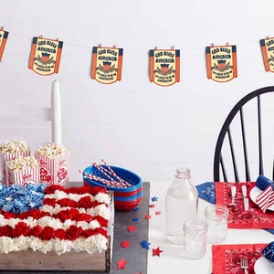 May include: A table setting for a patriotic party with red, white, and blue decorations. The table is decorated with a red, white, and blue floral arrangement, popcorn in striped containers, and red and blue bandana napkins. A string of bunting with the text "God Bless America" hangs above the table.