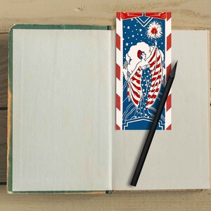 Peut inclure: Un carnet ouvert avec une page blanche &agrave; gauche et un marque-page &agrave; droite. Le marque-page est une illustration vintage d'une femme tenant un drapeau &agrave; rayures rouges, blanches et bleues. Le marque-page porte l'inscription "Liberty Bell".