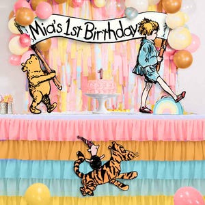 Puede incluir: Un conjunto de decoraci&oacute;n para una fiesta de primer cumplea&ntilde;os con tem&aacute;tica de Winnie the Pooh. El conjunto incluye una pancarta que dice "Mia's 1st Birthday", un personaje de Winnie the Pooh sosteniendo una pancarta, un personaje de Tigger y un personaje de Piglet. Las decoraciones est&aacute;n sobre una mesa con una falda de mesa de tul de tres niveles en rosa, amarillo y azul.