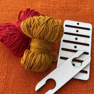 Peut inclure: Un écheveau de fil rouge, un écheveau de fil jaune moutarde, un outil de tissage rectangulaire en bois avec plusieurs fentes horizontales et de petits trous circulaires, et une navette en bois clair avec une encoche en U à chaque extrémité.