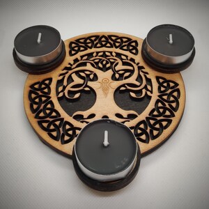 Könnte beinhalten: Ein Kerzenhalter aus Holz mit einem keltischen Knotenmuster und einem Lebensbaummotiv. Der Halter hat drei runde Plätze für Kerzen.