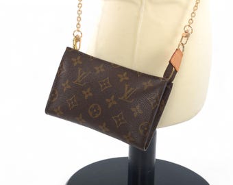 May include: A brown rectangular pouch featuring a repeating dark brown monogram pattern of the letters LV and floral motifs. The pouch has a gold-tone metal chain strap attached with light tan leather tabs and a top zipper closure.