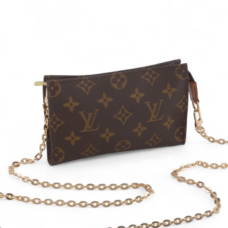 May include: Brown crossbody bag with a gold chain strap. The bag features a repeating pattern of brown logos on a brown background. The bag has a gold zipper and a gold chain strap.