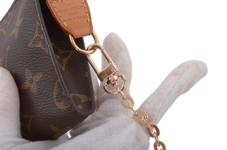 May include: Brown monogram canvas pouch with gold-tone hardware, including a chain strap and clasp. The pouch features a leather accent with the brand name. The design is classic and elegant.