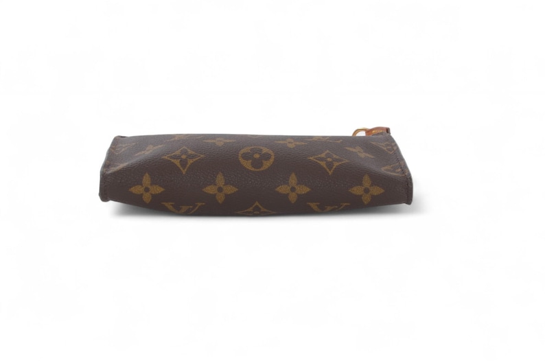 May include: Brown and tan zippered pouch with a repeating pattern of four-petal flowers and circles. The pouch is rectangular and has a brown zipper pull. The background is white.