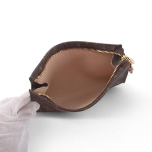 May include: Brown and tan zippered pouch with a gold-colored zipper. The interior is a light tan color. The pouch is held open by a gloved hand.