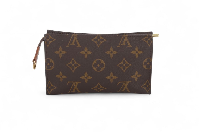 May include: Brown and tan rectangular pouch with a repeating pattern of interlocking floral and logo designs. The pouch has a gold-toned zipper and a small brown leather pull tab with a gold-toned ring. The pouch is likely made of leather.