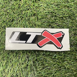 May include: A white sticker with black and red lettering that says "LTX". The "X" is a red slash with a white outline.