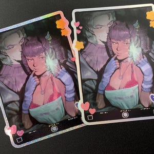 Könnte beinhalten: Zwei holografische Aufkleber mit einer digitalen Illustration eines Paares. Die Frau hat lila Haare, einen rosa BH und eine blaue Schürze. Der Mann steht hinter ihr und umarmt sie. Die Aufkleber sind mit Herzen und Sternen verziert.