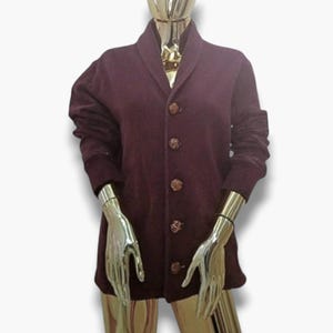 Op de afbeelding: Een bordeauxrode cardigan met een shawlkraag en vijf bruine knopen. De cardigan heeft lange mouwen en een ontspannen pasvorm.