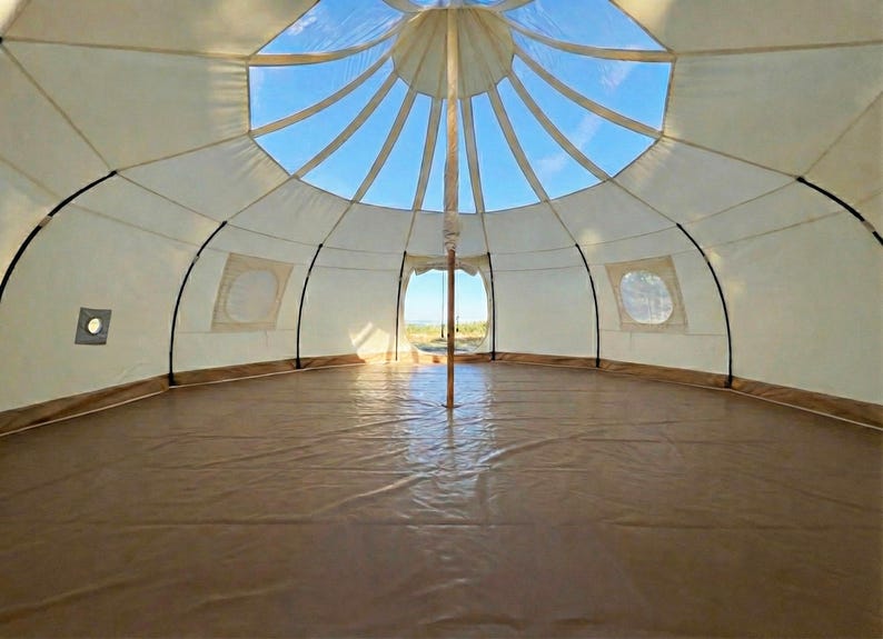 Spacious interior of the glamping tent with an outer wall height of 5 feet expaning to over 10 feet in the middle. Multiple windows, a stove jack, a large door, and a stunning transparent skylight offering beautiful views of the sky.