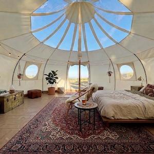 Spacious interior of the glamping tent stylishly furnished demonstrating its large interior. Multiple windows, a stove jack, a large door, and a stunning transparent skylight offering beautiful views of the sky.