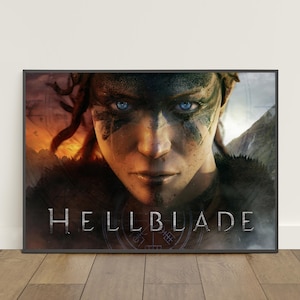 Puede incluir: Póster enmarcado con la palabra "HELLBLADE" en letras plateadas. La imagen es un primer plano de una persona con ojos azules y pintura facial. El fondo muestra un paisaje de fuego y una cordillera.