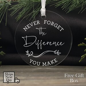 Peut inclure: Ornement de No&euml;l rond en acrylique transparent avec le texte "N'oubliez jamais la diff&eacute;rence que vous faites" en lettres blanches.