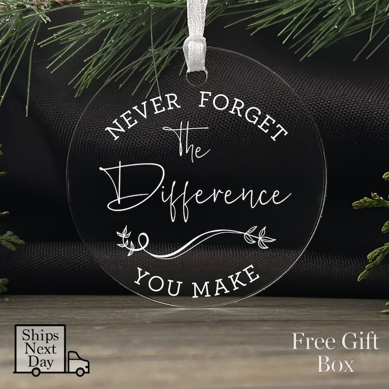 Peut inclure: Ornement de No&euml;l rond en acrylique transparent avec le texte "N'oubliez jamais la diff&eacute;rence que vous faites" en lettres blanches.