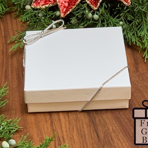 Peut inclure: Une bo&icirc;te cadeau blanche avec un ruban argent&eacute; nou&eacute; en forme de n&oelig;ud. La bo&icirc;te est pos&eacute;e sur une surface en bois. Free Gift Box est &eacute;crit sur une bo&icirc;te cadeau rouge et blanche.