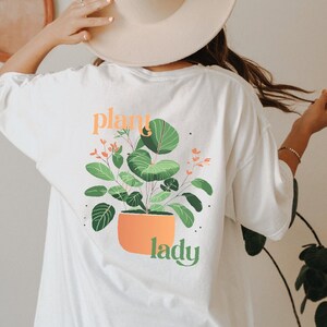 May include: White oversized t-shirt with a green plant graphic and the text "plant lady" on the back.
