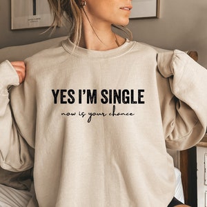 May include: A beige sweatshirt with the text "YES I'M SINGLE now is your chance" printed in black.